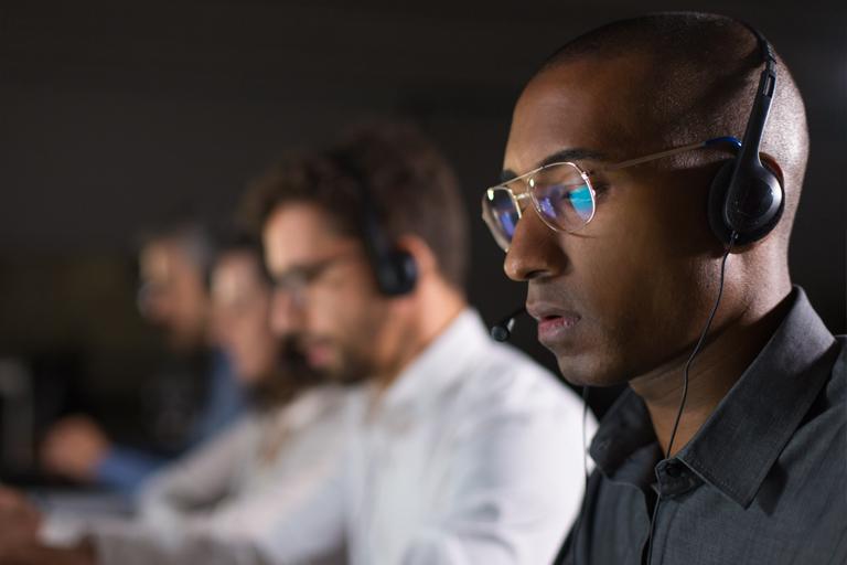 Man wearing glasses and headphones next to coworkers