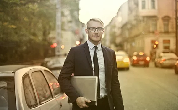 Man holding laptop standing next to a car on a busy city street