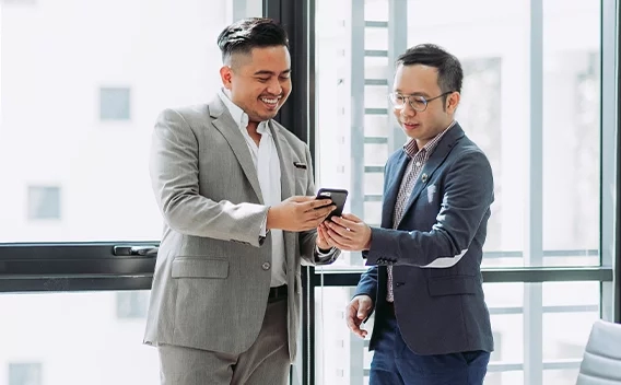 Two men looking at a phone standing in front of a window